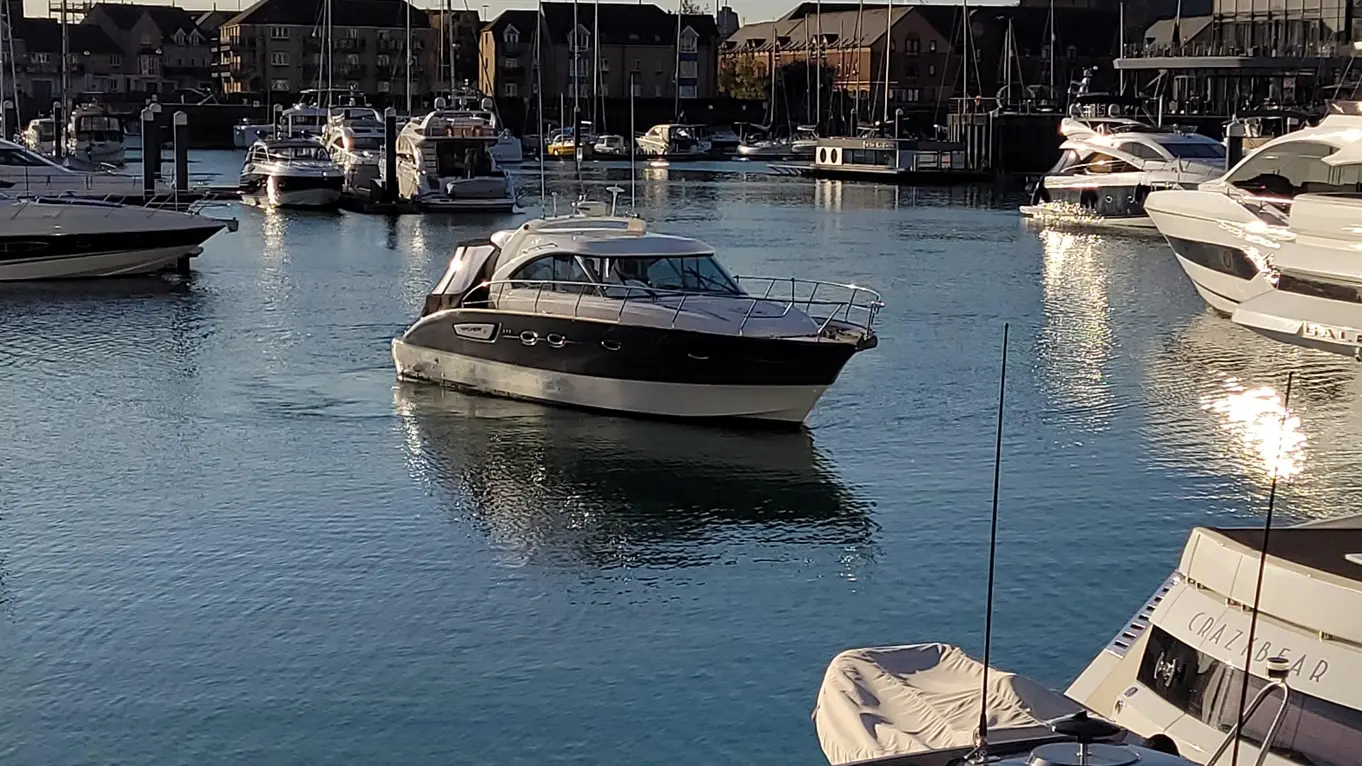 A motorboat navigates a marina filled with yachts and reflections on the water, highlighting a serene evening scene.